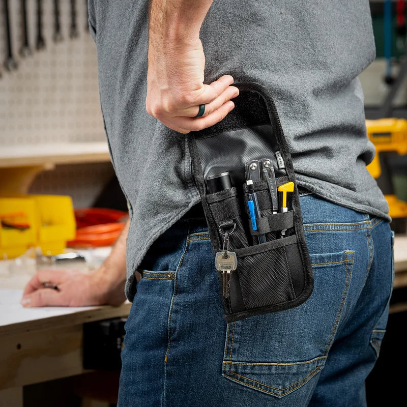 HOLSTERS - CLIP POCK-ITS XL - UTILITY black clip-on holster worn on hip of blue jeans, holding a flashlight, blue pen, screwdrivers, and key ring in workshop setting.