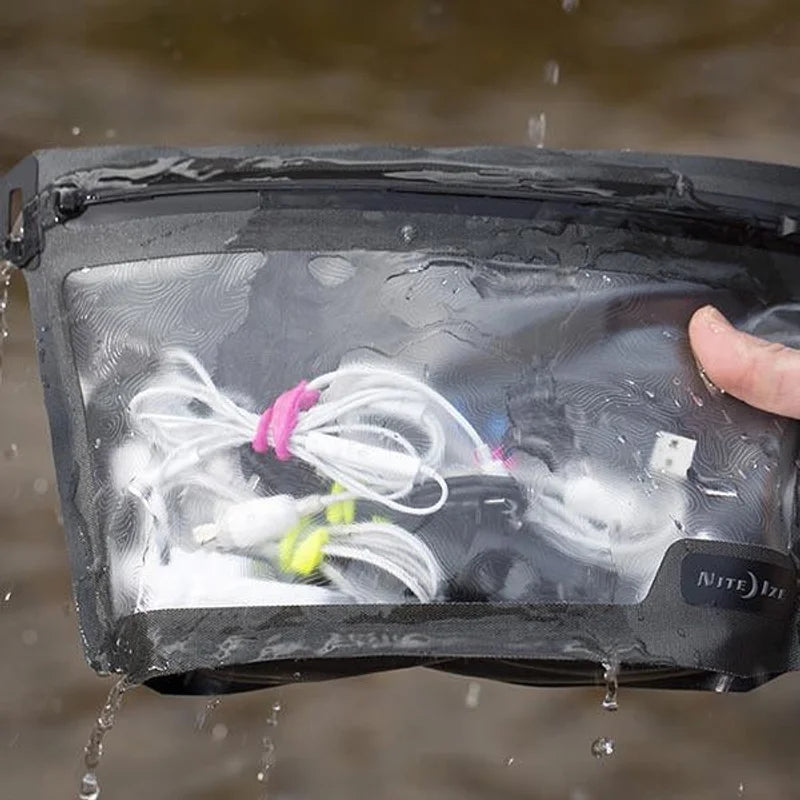 Nite Ize Waterproof Pouch black with clear front window showing white earbuds inside, water droplets on surface, hand holding pouch near water background.